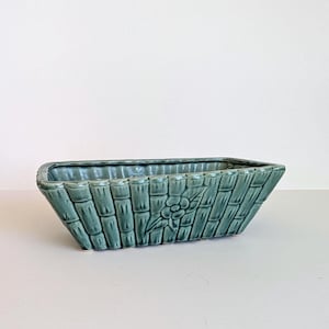 May include: A rectangular, teal ceramic planter with a woven bamboo design. The planter has a floral motif on one side. Suitable for indoor or outdoor use, it's a decorative item for plants. Measurements are in centimetres.