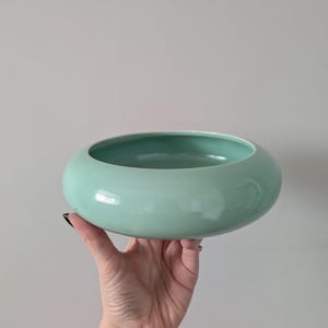 Peut inclure: Un bol rond en céramique vert menthe avec une finition lisse et brillante. Le bol est tenu dans une main sur un fond neutre. L'intérieur du bol est d'une nuance de vert légèrement plus foncée.