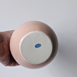 Op de afbeelding: Roze keramische vaas met een witte basis en een blauwe "Made in Japan" sticker op de bodem.