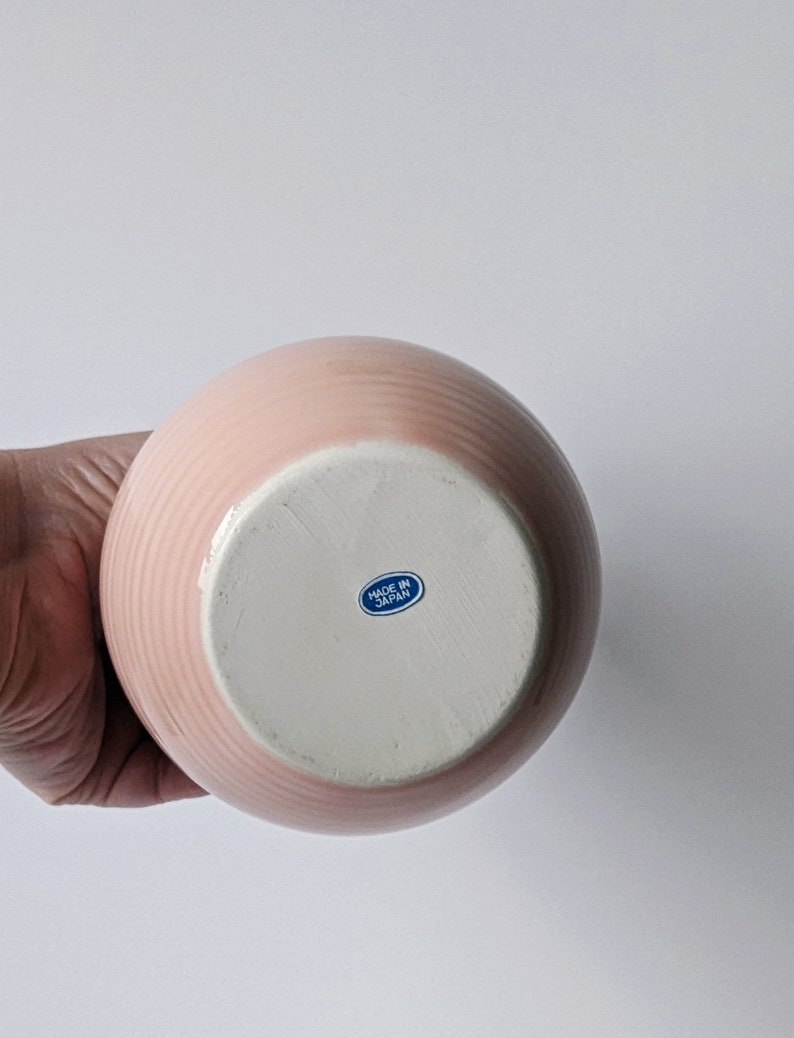 Op de afbeelding: Roze keramische vaas met een witte basis en een blauwe "Made in Japan" sticker op de bodem.