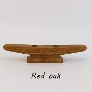 Puede incluir: Una cornamusa de madera de roble rojo, con una parte superior curvada y una base rectangular. Tiene dos agujeros. El texto "Red oak" está debajo. Ideal para aplicaciones náuticas.