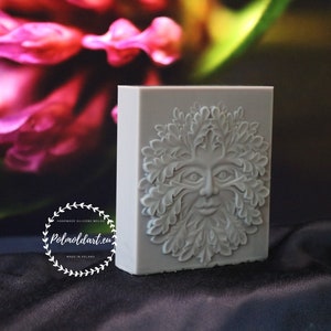 Può includere: Uno stampo rettangolare in silicone grigio chiaro con un rilievo dettagliato di un volto di Green Man circondato da foglie. Lo stampo ha una superficie liscia ed è posto su uno sfondo floreale sfocato. Il testo "Polmoldart.eu" è visibile.