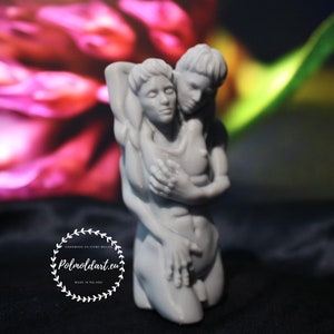 K&ouml;nnte beinhalten: Eine graue Skulptur, die zwei sich umarmende Figuren darstellt. Die Figuren sind nackt und in enger Umarmung. Die Skulptur befindet sich vor einem verschwommenen Hintergrund aus rosa und gr&uuml;nen Farbt&ouml;nen. Die Skulptur tr&auml;gt den Text "Polmoldart.eu" und "Handmade silicone molds" in einem kreisf&ouml;rmigen Design.