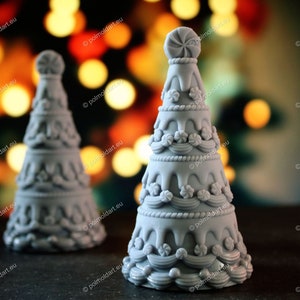 Könnte beinhalten: Zwei graue, dekorative Weihnachtsbaumfiguren mit aufwendigen Details. Die Bäume haben ein mehrschichtiges Design mit zuckerartigen Akzenten und bonbonförmigen Verzierungen. Der Hintergrund zeigt verschwommene, warmtonige Lichter.