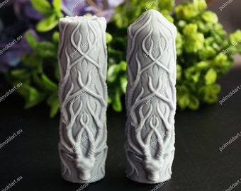 May include: Two gray, cylindrical molds with intricate, raised designs. Each mold features a deer-like head at the base and a pattern of intertwined branches and leaves. The molds are for crafting decorative items.