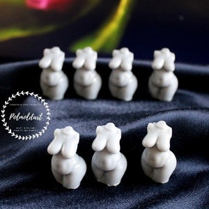 Puede incluir: Una colecci&oacute;n de peque&ntilde;as esculturas de torso femenino grises dispuestas sobre una superficie oscura y texturizada. Las esculturas est&aacute;n estilizadas y tienen formas redondeadas. La imagen incluye un logotipo con el texto "Polmoldart" en un dise&ntilde;o circular.