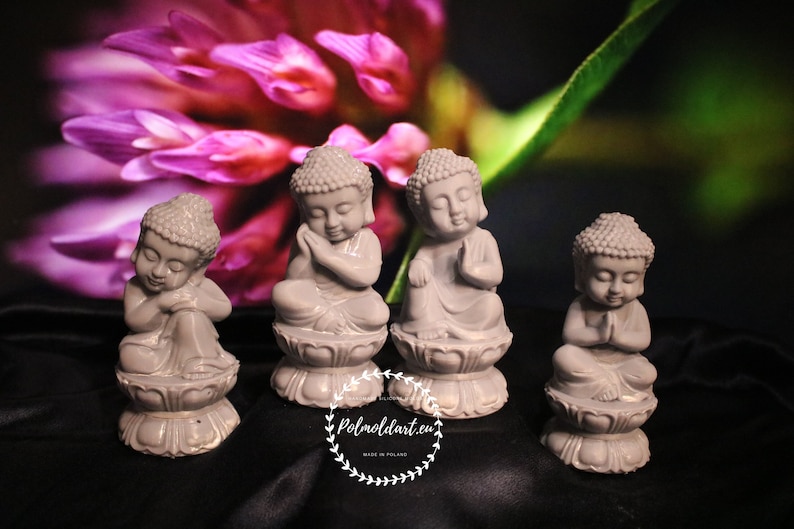 May include: Four small gray Buddha statues in various poses, seated on lotus flower bases. The statues have serene expressions and are set against a blurred background of pink and green.