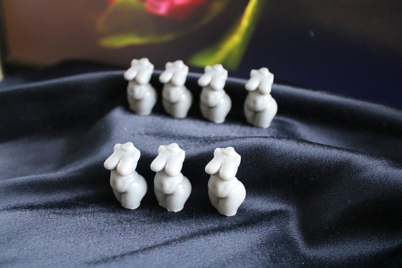 Puede incluir: Ocho peque&ntilde;as figuras de torso femenino grises est&aacute;n dispuestas sobre una tela azul oscuro y sedosa. Las figuras est&aacute;n estilizadas con formas redondeadas y superficies lisas, lo que sugiere una est&eacute;tica minimalista.