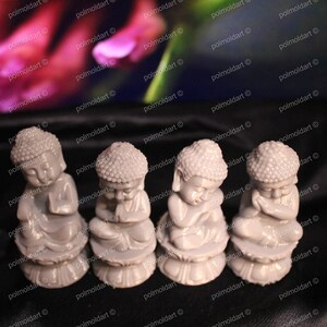 May include: Four small, gray Buddha statues in a row, each in a seated pose with hands clasped in prayer. The statues have detailed features and sit on a lotus flower base. The background is blurred with pink and green hues.