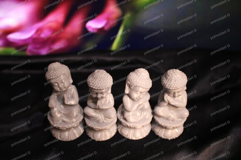 May include: Four small, gray Buddha statues in a row, each in a seated pose with hands clasped in prayer. The statues have detailed features and sit on a lotus flower base. The background is blurred with pink and green hues.