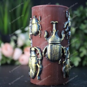 Pu&ograve; includere: Una candela cilindrica marrone decorata con decorazioni a forma di scarabeo dorato. Gli scarabei presentano dettagli intricati e una lucentezza metallica. La candela &egrave; un oggetto decorativo, adatto per l'arredamento della casa o come regalo unico.