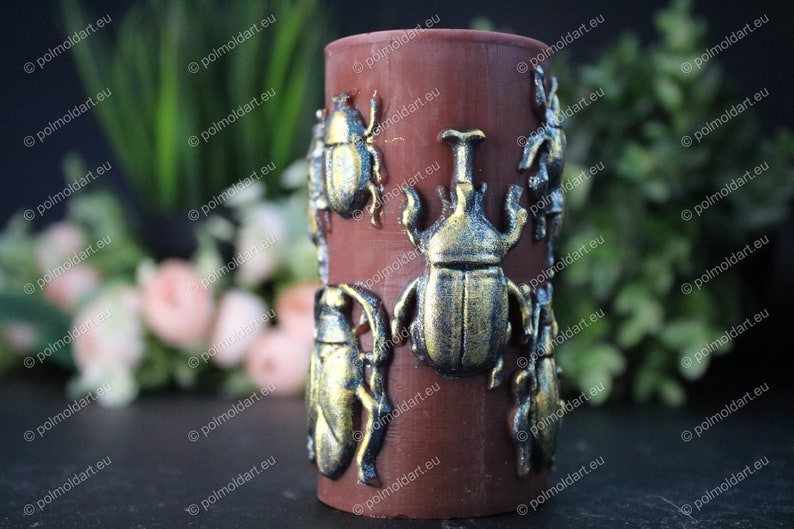 Pu&ograve; includere: Una candela cilindrica marrone decorata con decorazioni a forma di scarabeo dorato. Gli scarabei presentano dettagli intricati e una lucentezza metallica. La candela &egrave; un oggetto decorativo, adatto per l'arredamento della casa o come regalo unico.