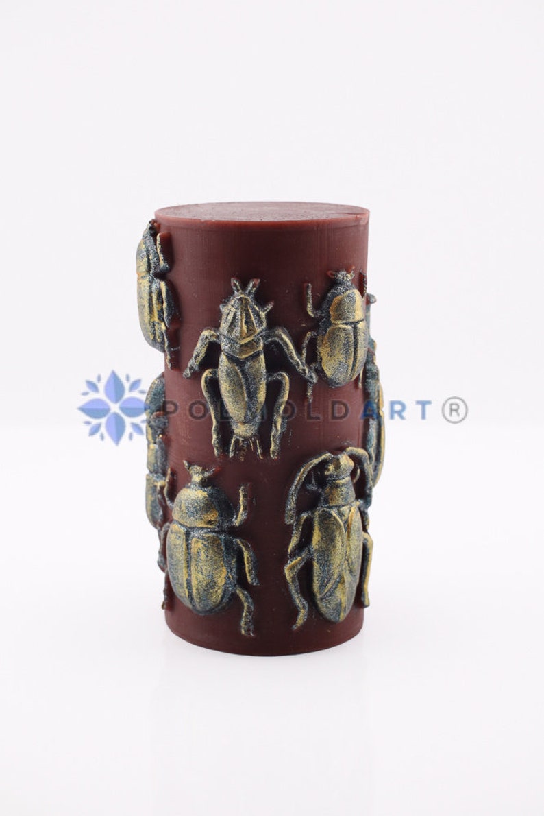 Pu&ograve; includere: Una candela cilindrica bordeaux con disegni di scarabei dorati e blu in rilievo. La candela presenta un motivo ripetuto di figure di insetti dettagliate, creando un elemento decorativo unico. Un elemento decorativo per la casa.