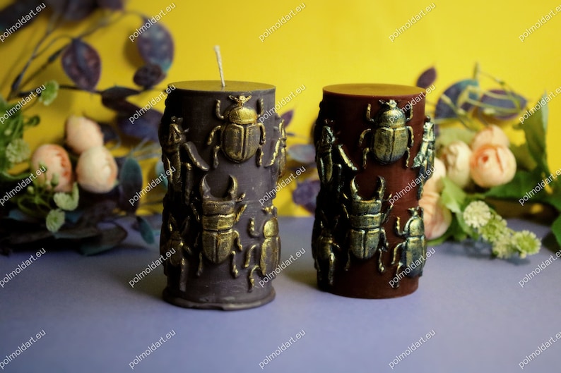 Pu&ograve; includere: Due candele a colonna decorative. Una &egrave; viola scuro, l'altra marrone rossiccio. Entrambe sono decorate con abbellimenti a forma di scarabeo dorato. Le candele hanno un aspetto rustico e strutturato e sono su uno sfondo floreale giallo e viola.