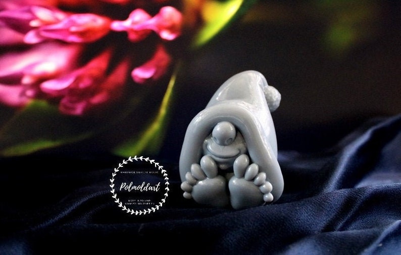 May include: A gray gnome figurine with a pointed hat and large feet. The gnome is smiling and appears to be hiding under its hat. The figurine is made of a smooth material and is set against a dark blue background.