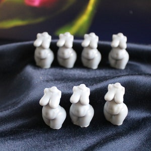 Puede incluir: Una colecci&oacute;n de ocho peque&ntilde;as esculturas de torso femenino de color gris claro. Las esculturas est&aacute;n dispuestas en dos filas sobre una tela azul oscuro. Las esculturas son lisas y tienen un dise&ntilde;o minimalista.