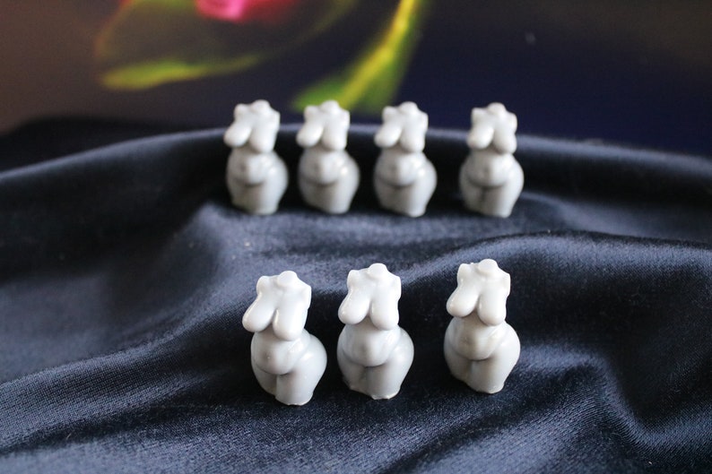 Puede incluir: Una colecci&oacute;n de ocho peque&ntilde;as esculturas de torso femenino de color gris claro. Las esculturas est&aacute;n dispuestas en dos filas sobre una tela azul oscuro. Las esculturas son lisas y tienen un dise&ntilde;o minimalista.