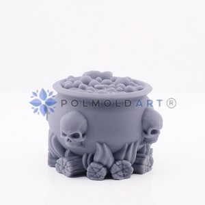 May include: A grey cauldron-shaped ornament featuring three skulls and a bubbling top. The cauldron has a textured surface and is decorated with stylized flames and pinecone-like shapes at the base. The text "POLMOLDART®" is visible.