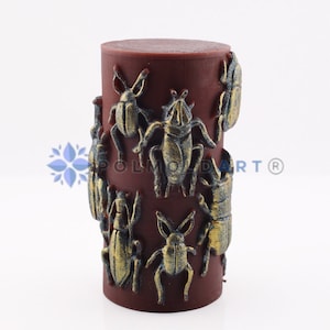 Pu&ograve; includere: Una candela cilindrica bordeaux decorata con disegni di scarabei dorati in rilievo. La candela ha una superficie liscia ed &egrave; adornata da varie forme di insetti, creando un pezzo decorativo unico.