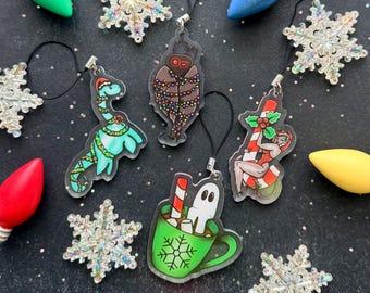May include: A collection of acrylic ornaments featuring a green dinosaur with Christmas lights, a moth wrapped in lights, a figure on a candy cane, and a ghost in a green mug, surrounded by iridescent snowflake ornaments and colorful light bulbs.