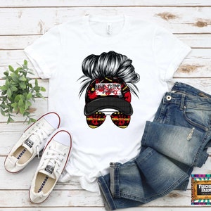 May include: White t-shirt with a graphic of a woman's hair in a bun wearing a black baseball cap with the text "True Crime Junkie" in red and white. The woman is wearing sunglasses with yellow and black tape.