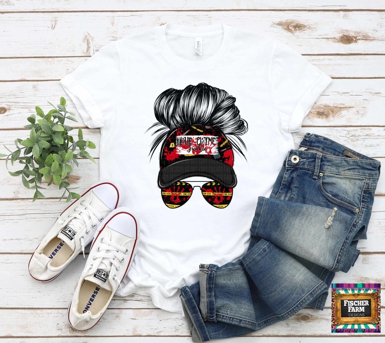 May include: White t-shirt with a graphic of a woman's hair in a bun wearing a black baseball cap with the text "True Crime Junkie" in red and white. The woman is wearing sunglasses with yellow and black tape.