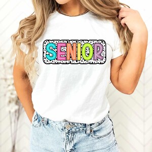 May include: White t-shirt with a colorful "SENIOR" graphic with black polka dots. The graphic has a white outline and is surrounded by a black polka dot border.