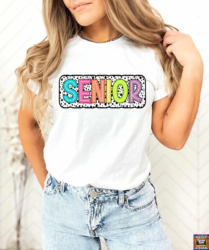 May include: White t-shirt with a colorful "SENIOR" graphic with black polka dots. The graphic has a white outline and is surrounded by a black polka dot border.