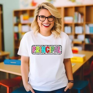 May include: A white t-shirt with a colorful "PRINCIPAL" graphic on the front. The graphic is surrounded by black polka dots and has a black outline.