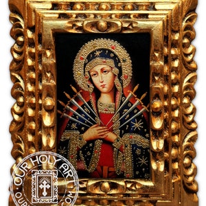 Puede incluir: Icono religioso enmarcado que representa a una mujer con halo, vestida con una túnica roja y azul, con siete espadas que le atraviesan el pecho. El marco dorado ornamentado tiene tallas detalladas. La imagen tiene el texto "OUR HOLY ART.COM".