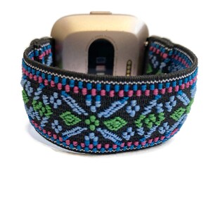 May include: A black watch band with a colorful geometric pattern. The band is made of elastic material and has a woven design with blue, green, pink, and white accents.