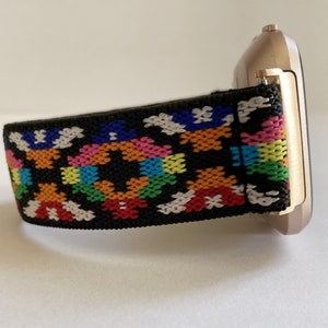 May include: A black watch band with a colorful geometric pattern. The band is made of a soft, stretchy material and is compatible with smartwatches.