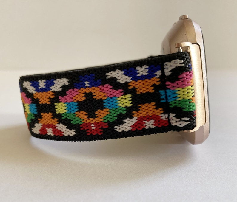 May include: A black watch band with a colorful geometric pattern. The band is made of a soft, stretchy material and is compatible with smartwatches.