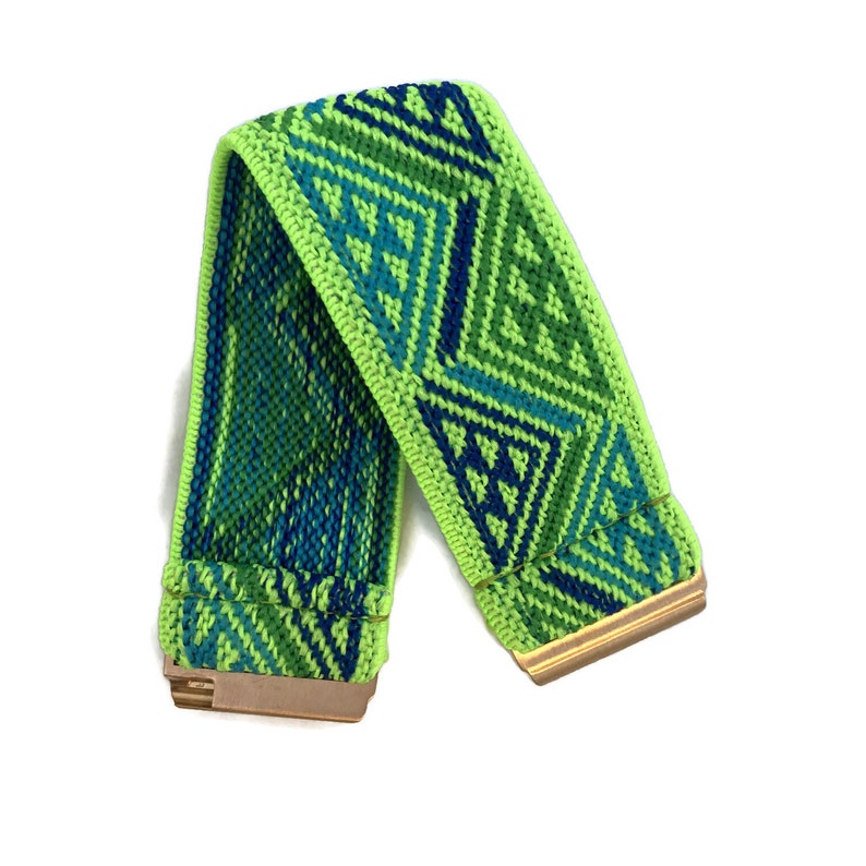 May include: A green elastic headband with a geometric pattern in shades of blue and green. The headband has gold metal ends.