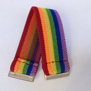 May include: A rainbow-striped elastic band with silver-colored metal clasps. The band features a vibrant spectrum of colors, including red, orange, yellow, green, blue, and purple. The band is designed to be worn as a bracelet or accessory.