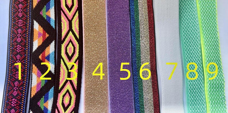 May include: A collection of nine colorful elastic bands. The bands feature various patterns, including geometric designs and solid colors. The colors include pink, brown, blue, yellow, gold, purple, green, white, and light green. These bands are suitable for various crafting projects.