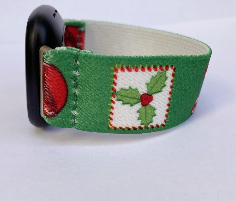 Puede incluir: Una banda de reloj de tem&aacute;tica navide&ntilde;a verde y blanca con un dise&ntilde;o de bayas de acebo rojas. La banda est&aacute; hecha de tela y tiene un respaldo el&aacute;stico blanco.