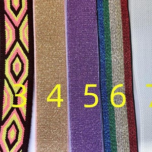 Könnte beinhalten: Eine Sammlung von neun farbenfrohen elastischen Bändern. Die Bänder weisen verschiedene Muster auf, darunter geometrische Designs und unifarbene Farben. Die Farben umfassen Rosa, Braun, Blau, Gelb, Gold, Lila, Grün, Weiß und Hellgrün. Geeignet für verschiedene Bastelprojekte.