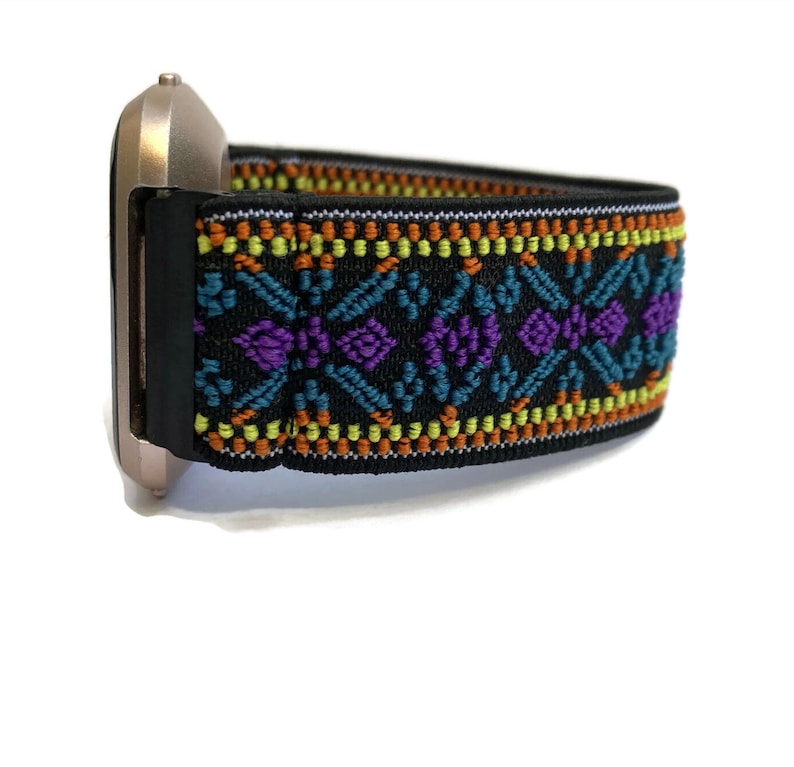 K&ouml;nnte beinhalten: Ein schwarzes Uhrenarmband mit einem farbenfrohen geometrischen Muster in Orange, Gelb, Blau und Lila. Das Armband ist aus elastischem Material und hat ein gewebtes Design.