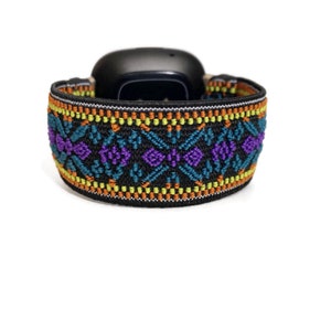 May include: A black fitness tracker with a colorful patterned band. The band features a geometric design with orange, yellow, teal, and purple accents.