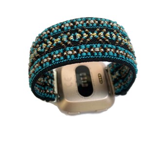 May include: A gold-colored smartwatch with a black and blue patterned band. The band has a geometric design with brown, white, and blue threads.