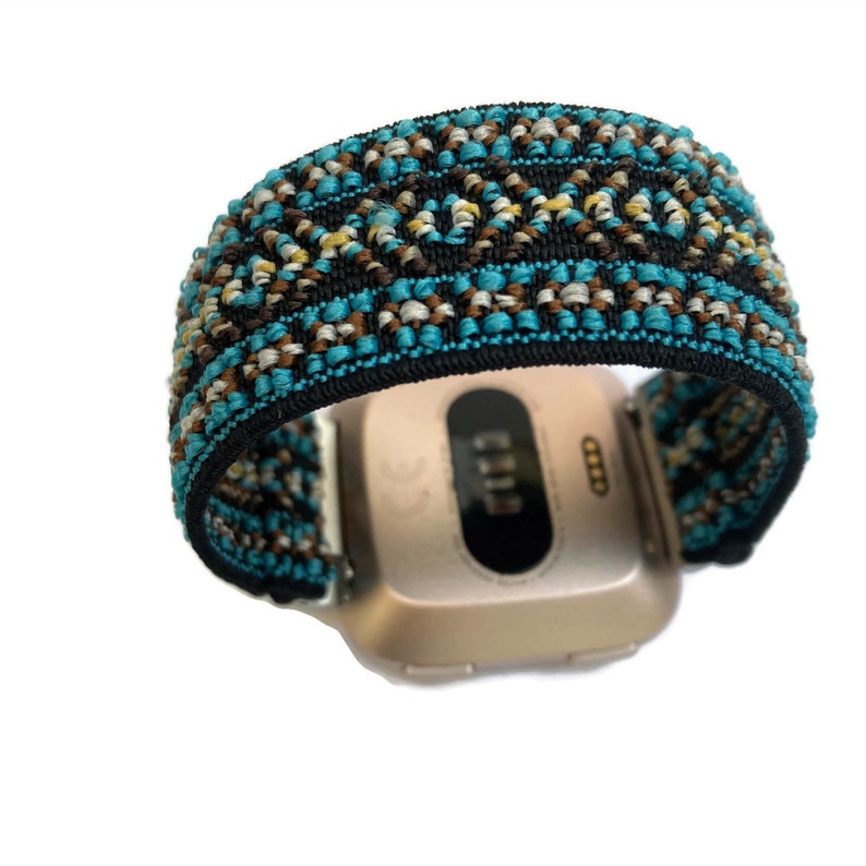 May include: A gold-colored smartwatch with a black and blue patterned band. The band has a geometric design with brown, white, and blue threads.
