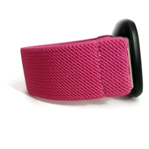 May include: A pink elastic band with a black round device attached to it. The band is made of a woven fabric.