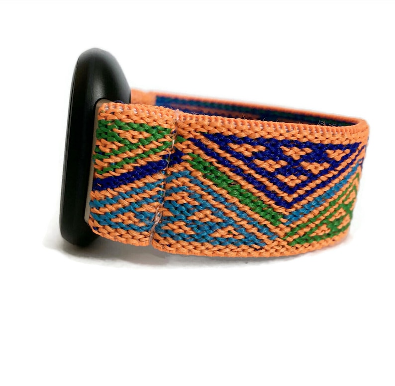 May include: A woven watch band with a geometric pattern in shades of orange, blue, and green. The band is made of a soft, stretchy material and has a black buckle.