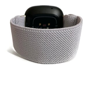 May include: A gray sport band for a smartwatch. The band is made of a soft, stretchy material and has a textured surface.