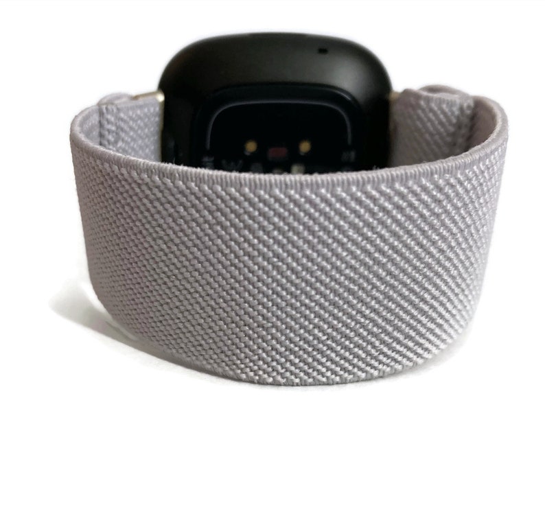 May include: A gray sport band for a smartwatch. The band is made of a soft, stretchy material and has a textured surface.