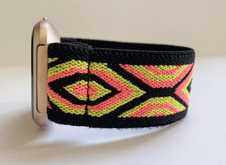 May include: A black elastic watch band with a geometric pattern in pink and yellow. The band is attached to a rose gold watch face.