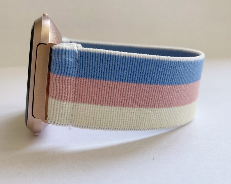 May include: A rose gold smartwatch with a blue, pink, and white striped elastic band.