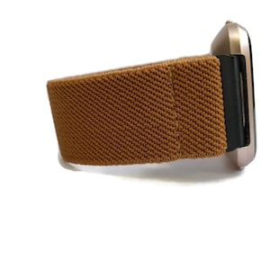 May include: A brown elastic watch band with a black buckle. The band is made of a soft, stretchy material and is designed to fit comfortably on the wrist.