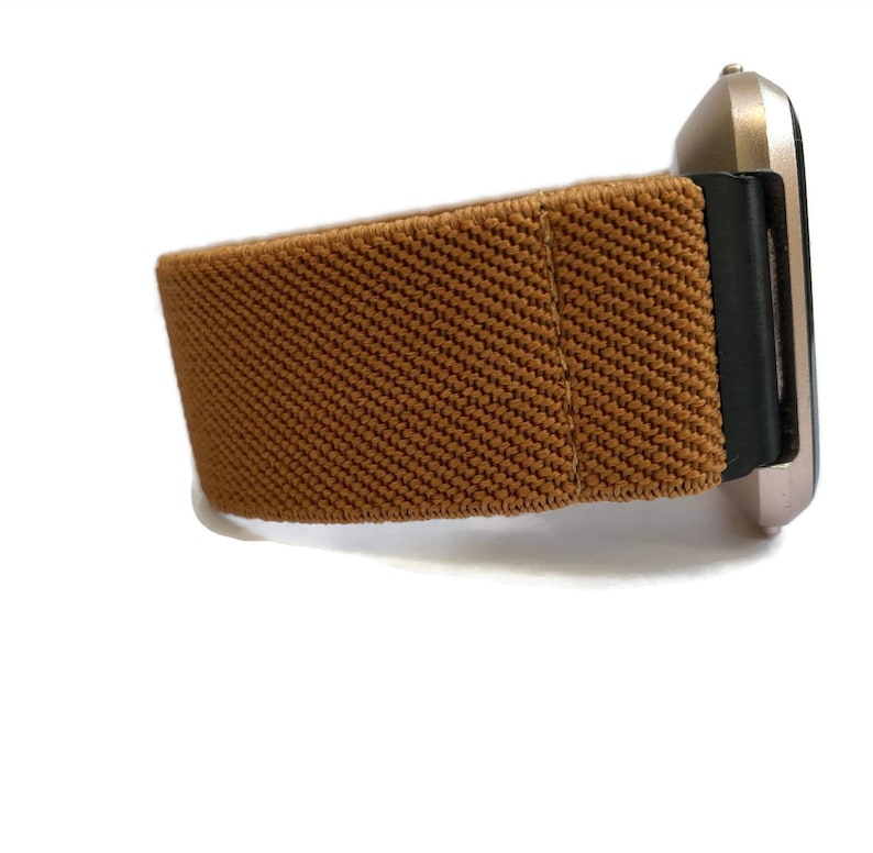 May include: A brown elastic watch band with a black buckle. The band is made of a soft, stretchy material and is designed to fit comfortably on the wrist.